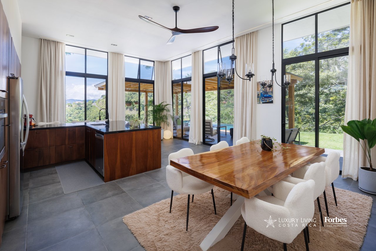 Open-plan kitchen and dining area with a wood dining table, dark cabinetry, and floor-to-ceiling windows.