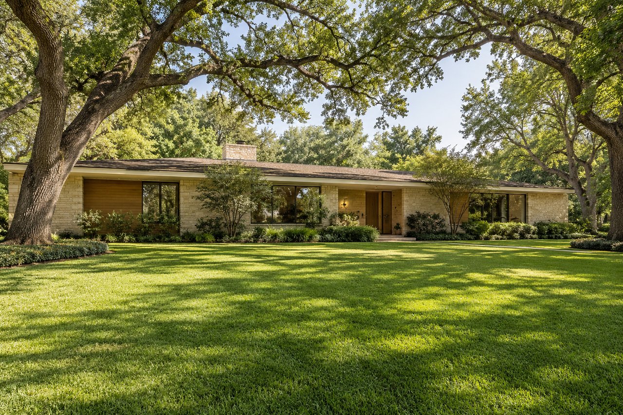Single-story stone home with broad windows and a central entrance beneath mature trees.
