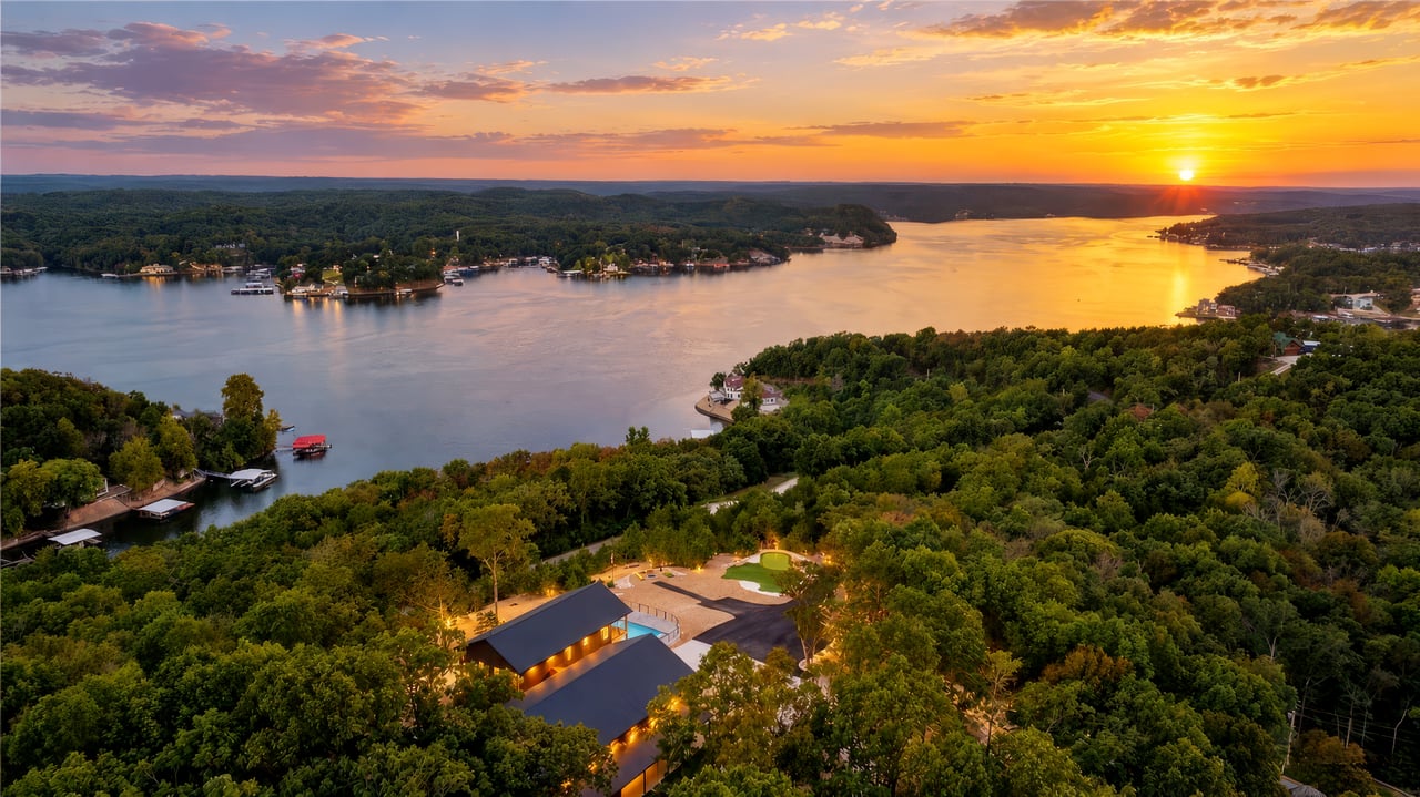 A wooded lake with homes and docks at sunset, viewed above a building complex and pool.