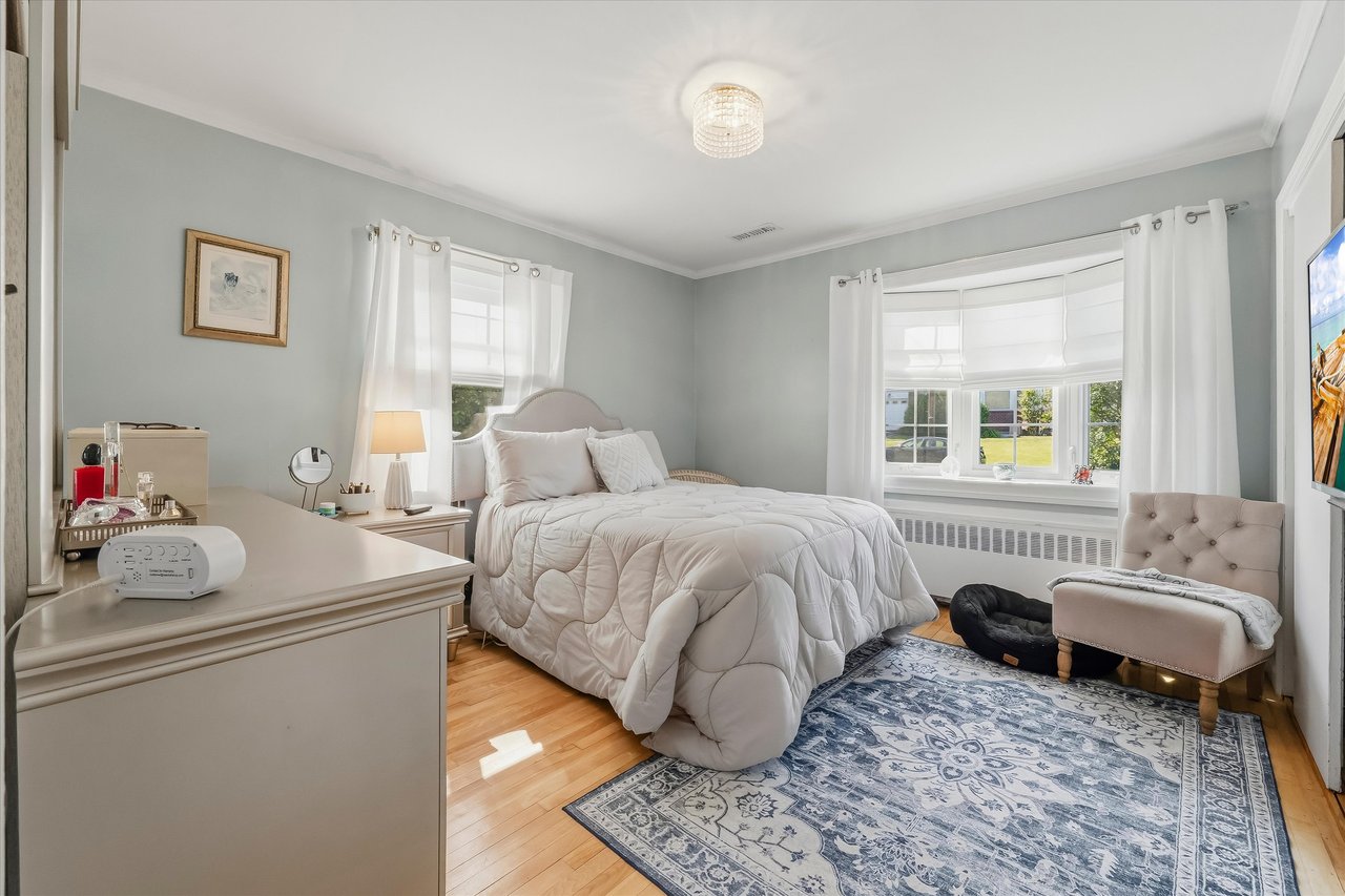 Bedroom with a white bed, bay window, hardwood floors, and blue patterned rug.