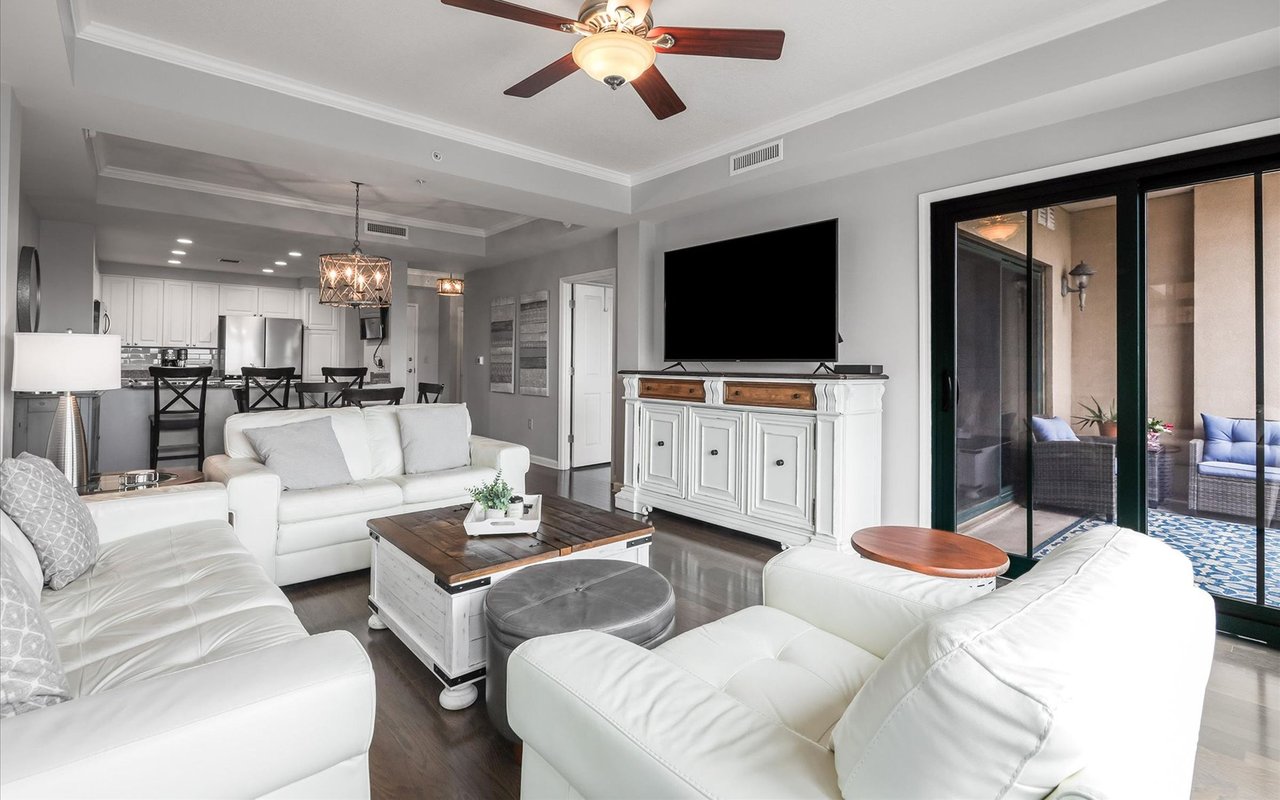 Open-plan living room with white sofas, a dark wood coffee table, and sliding glass doors to a patio.