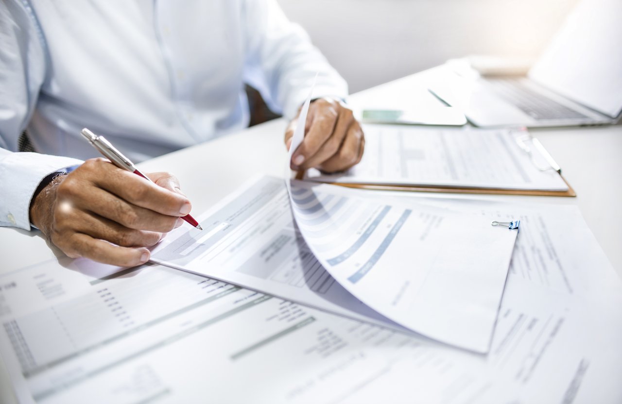 At a desk, a person is meticulously reviewing and marking documents with a red pen, perhaps organizing them for a home closing