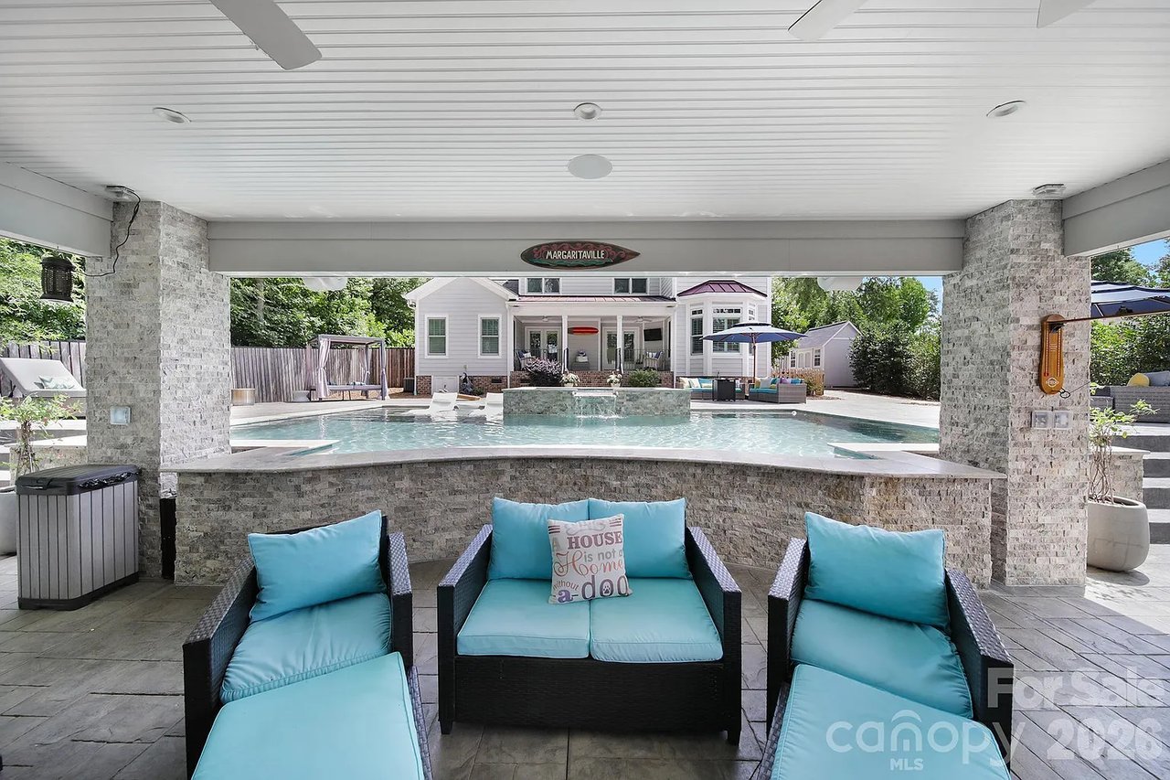 Covered patio with turquoise seating overlooking a swimming pool and house.