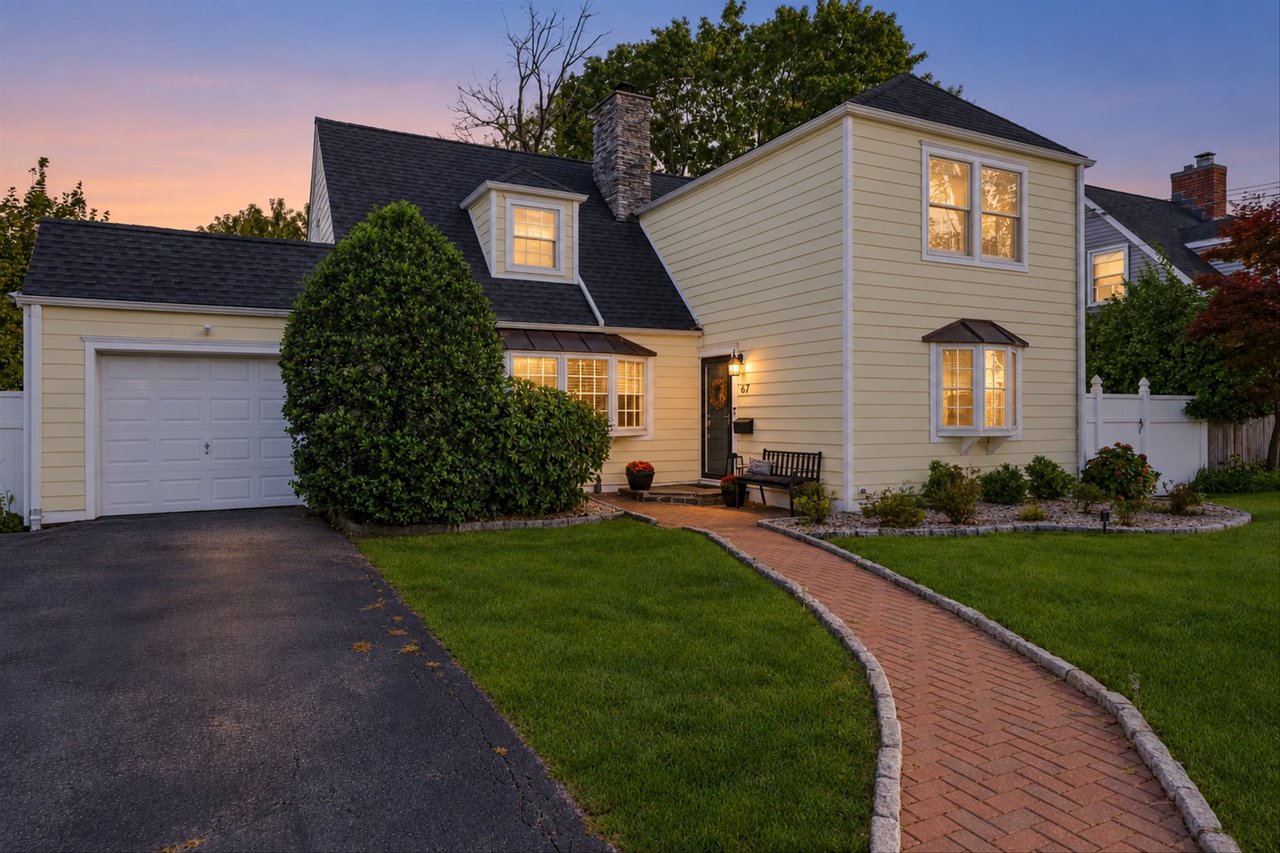 Cream two-story house at dusk with a stone chimney and curved brick walkway.