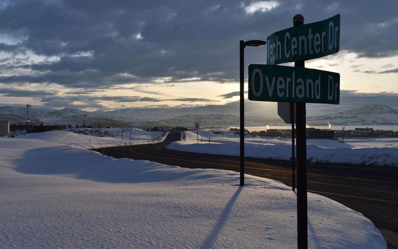 Snowy Kimball Junction road at sunset, marked by Tech Center Drive and Overland Drive signs.
