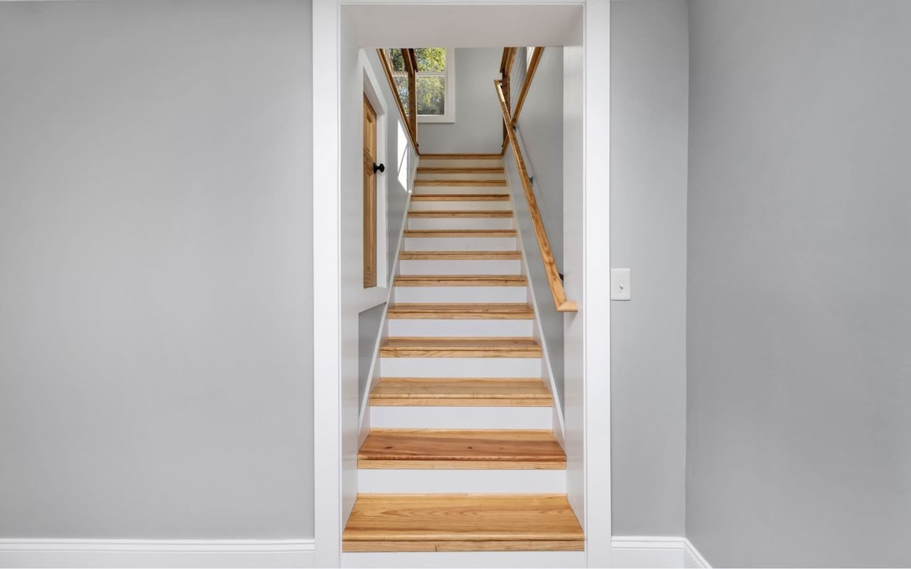 Modern home interior featuring an oak hardwood staircase with painted white risers, wood handrail, matching white trim work, and neutral grey painted walls.