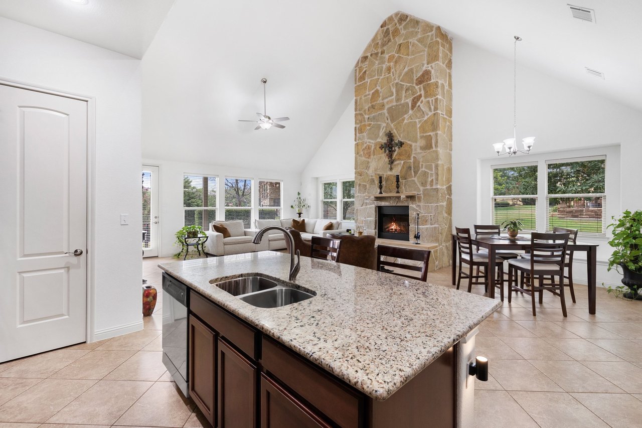 Open-plan kitchen with a granite island, tall stone fireplace, and dining area.