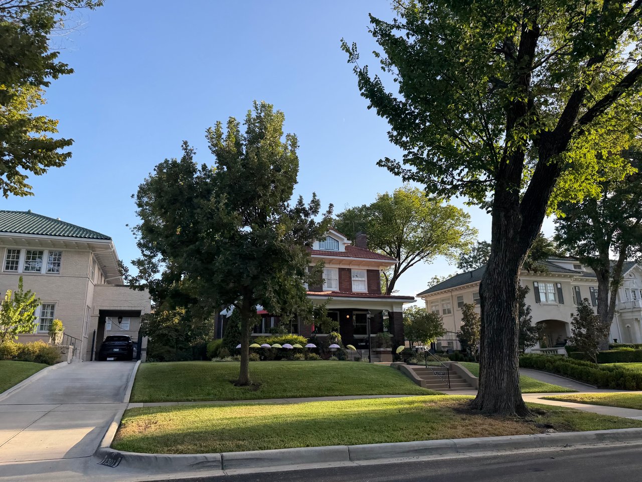 Two-story brick home with a covered porch, framed by mature trees and neighboring houses.