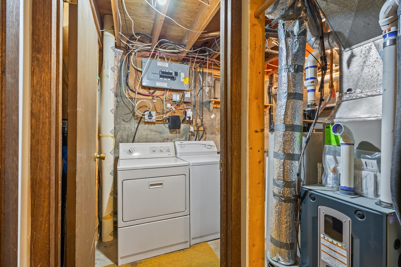 Basement laundry area with a washer and dryer beside exposed mechanical equipment and ductwork.