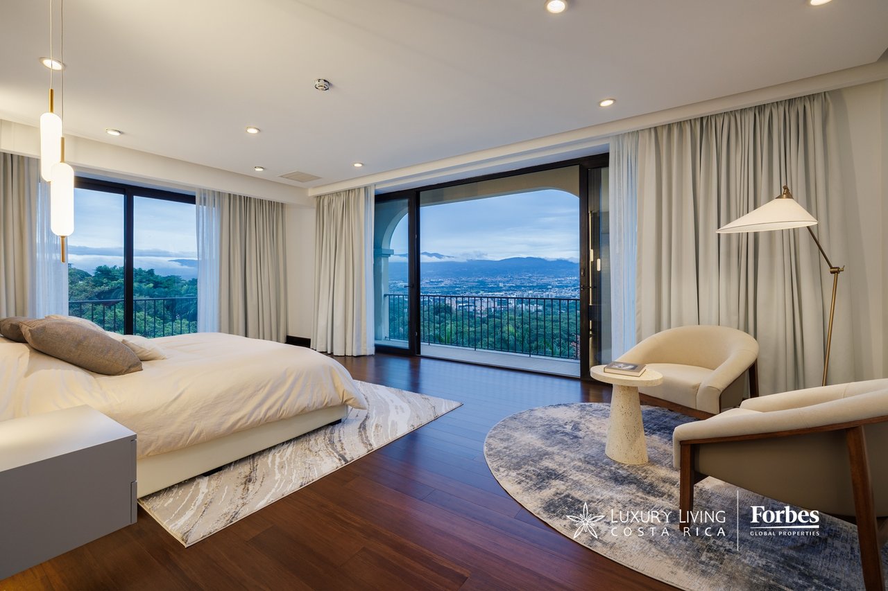 Penthouse bedroom with floor-to-ceiling windows overlooking the city and mountains.
