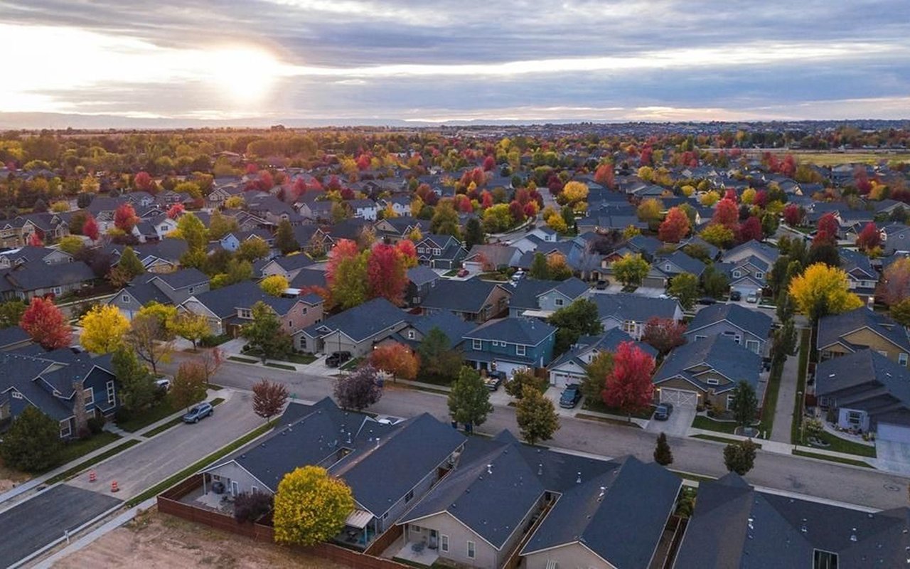 Aerial view of a suburban neighborhood with colorful autumn trees beneath a cloudy sunset.