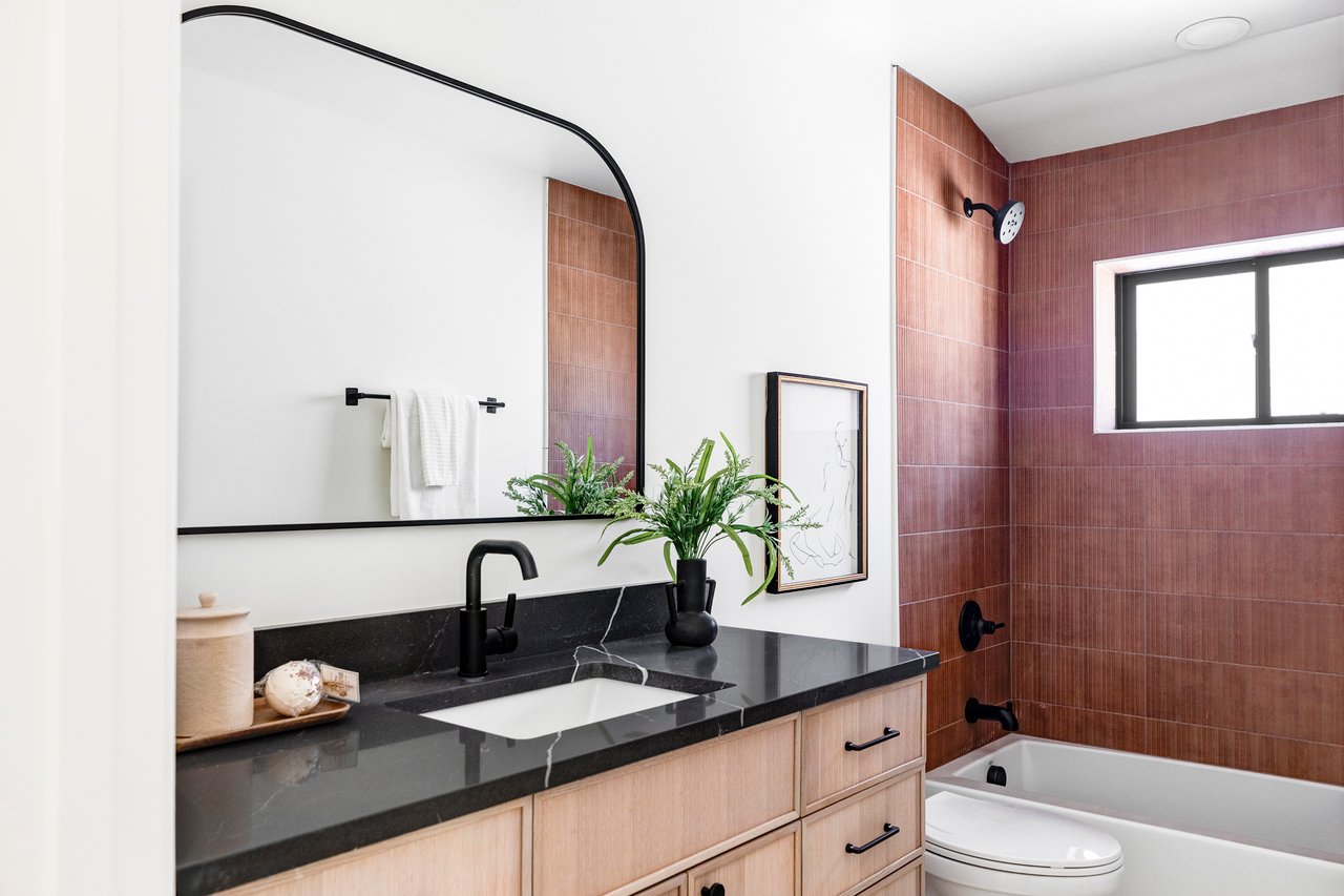 Full bathroom with one sink, quartz-top vanity and wood cabinets underneath. Shower and tub tiled with burgundy tile.