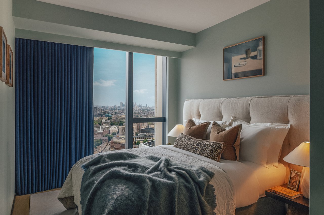 Furnished bedroom with a large bed and London skyline views through floor-to-ceiling windows.