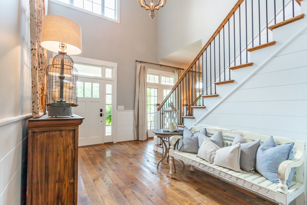 Bright home foyer with a white front door, wood staircase, and cushioned bench.