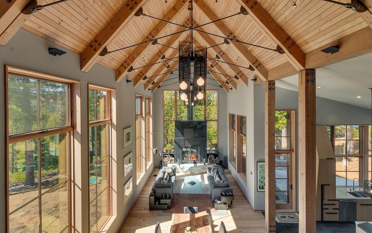 Furnished great room with a vaulted timber ceiling, tall windows, and a central fireplace.