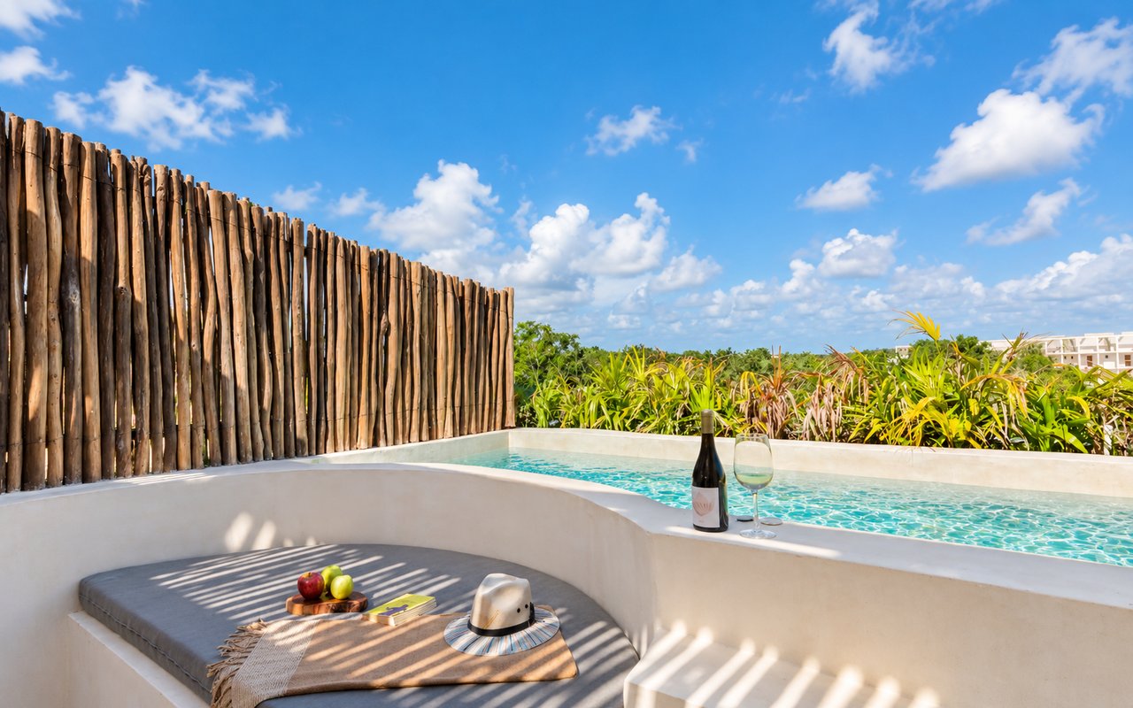 Plunge pool beside a curved sunken lounge, wooden privacy fence, and tropical plants.