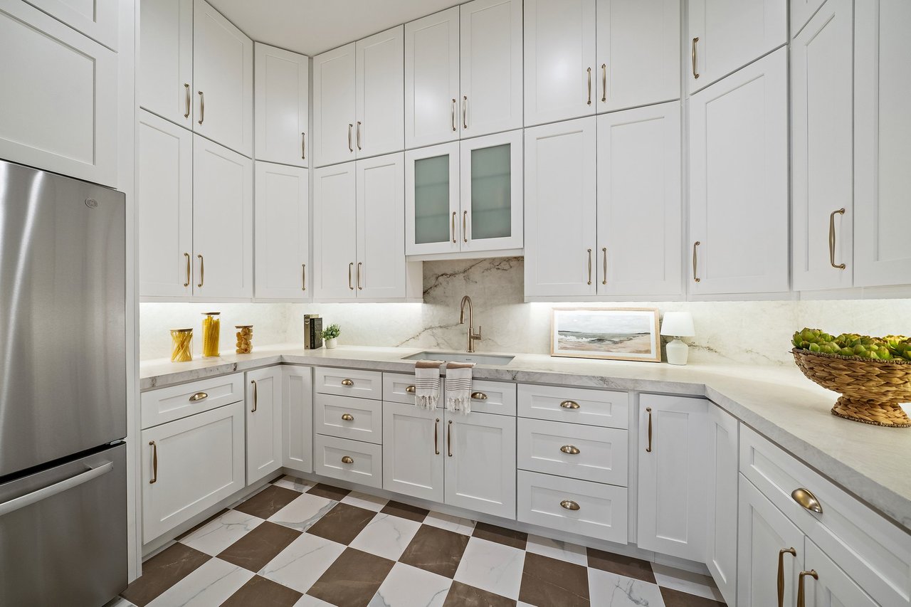Bright white kitchen with shaker cabinets, marble-look counters, stainless steel refrigerator, and checkerboard tile floor.