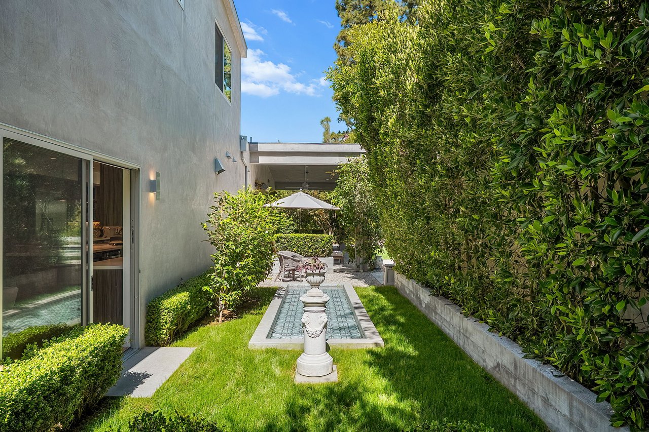 Modern home courtyard with a narrow fountain pool, clipped hedges, lawn, and covered patio.