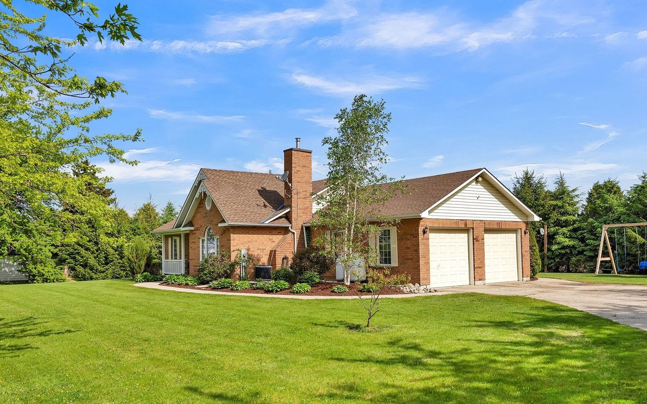 Red-brick house with an attached two-car garage, landscaped garden beds, and a broad green lawn.