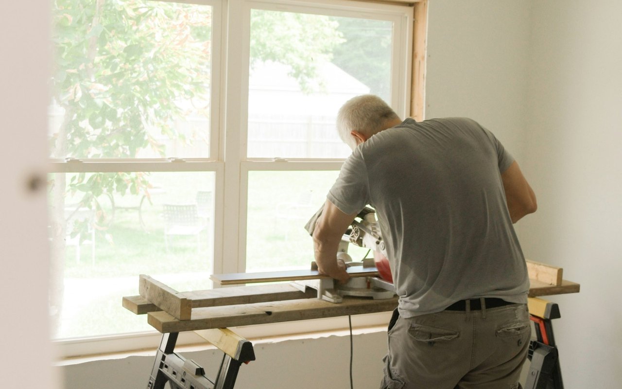 Worker cutting lumber on a saw station inside a home undergoing renovation.