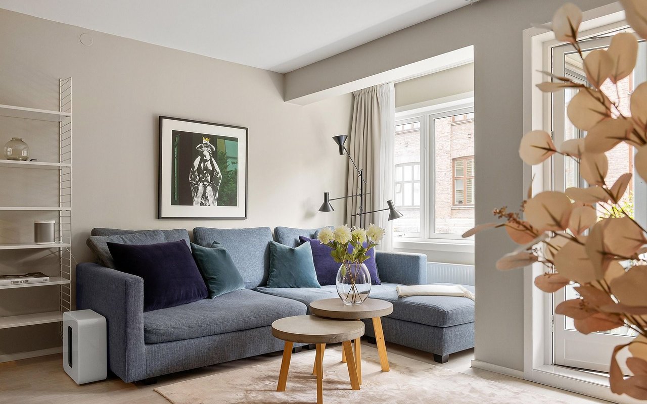 Furnished living room with a gray sectional, nested coffee tables, and large bright windows.