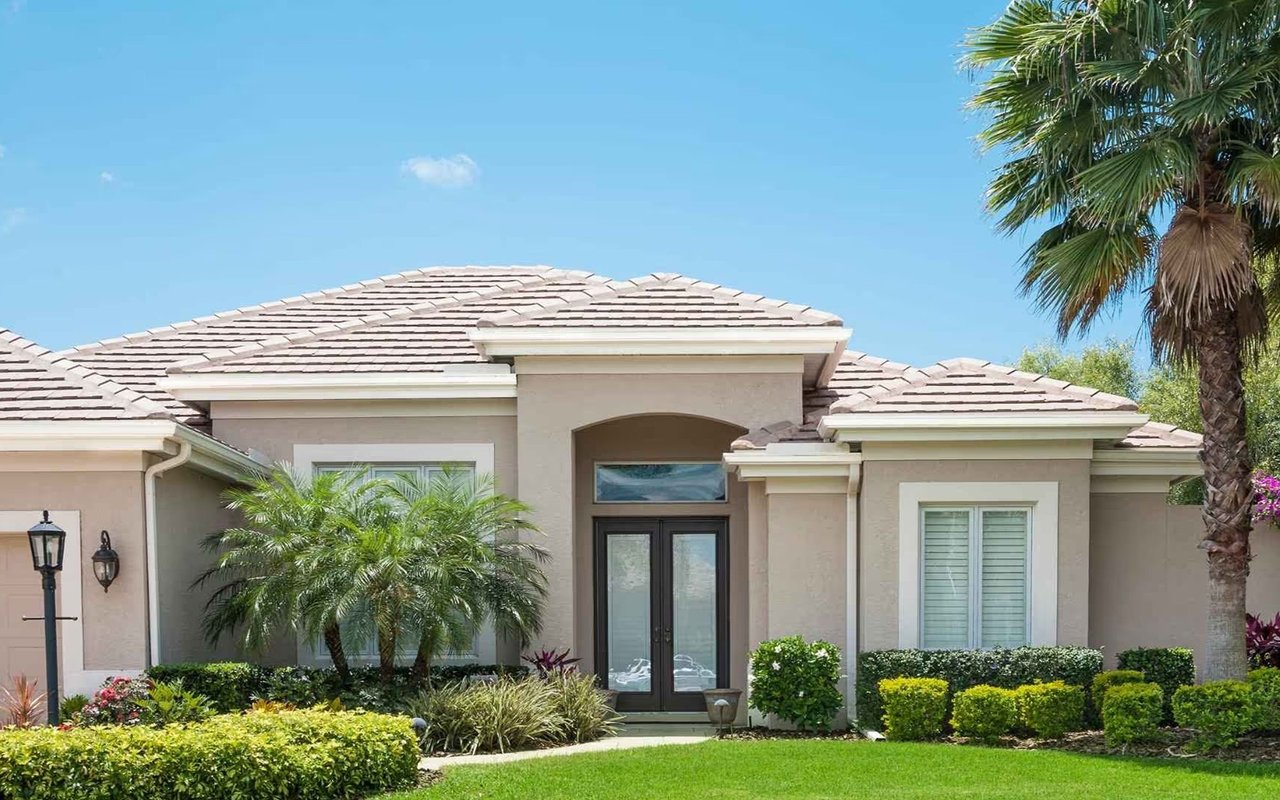 Single-story stucco home with a tiled roof, palm trees, and landscaped front lawn.