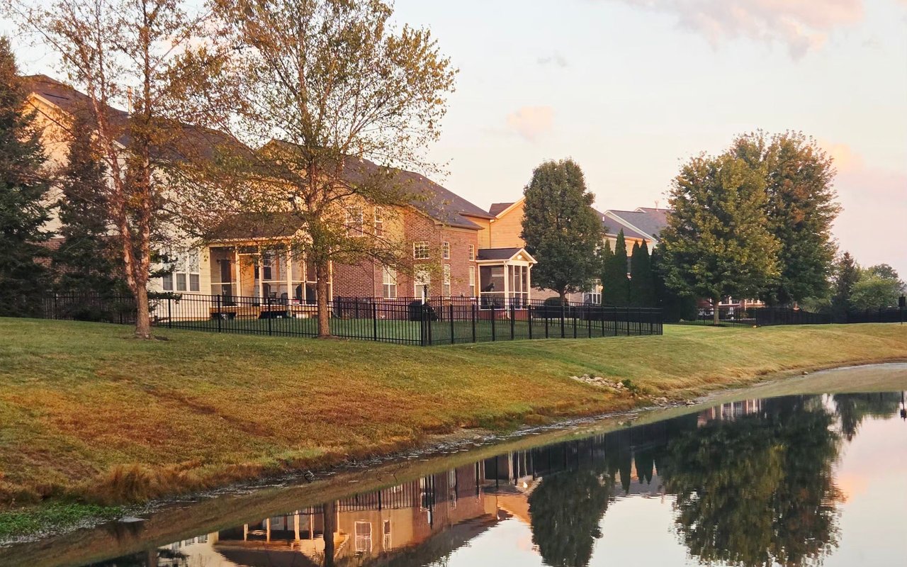 Suburban homes beside a pond, reflected in the water at golden hour.