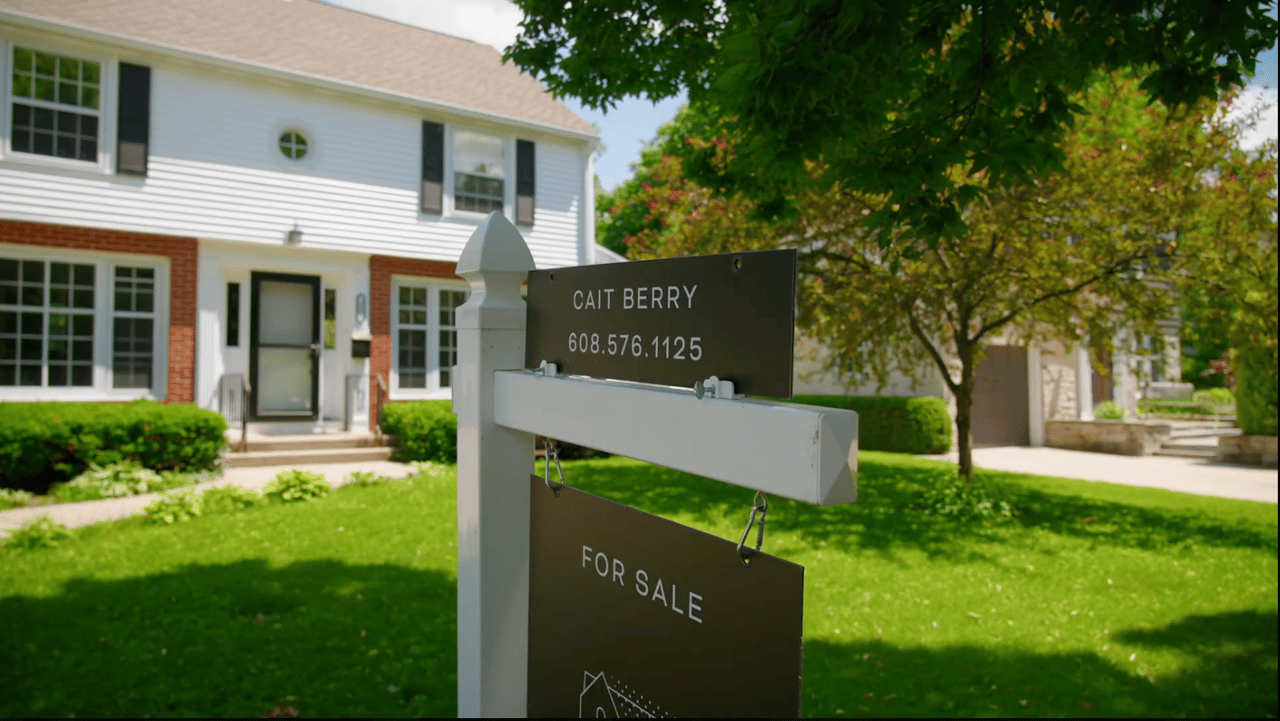 A Cait Berry of Insiders Realty For Sale sign staked in the front yard of a two-story white and brick Madison, Wisconsin home on a sunny day, representing a thoughtfully prepared home ready for the market.