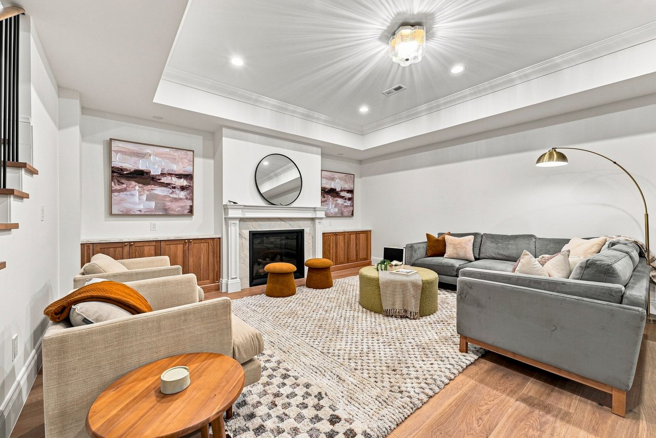 Living room with gray sectional, white fireplace, round mirror, and cream armchairs.