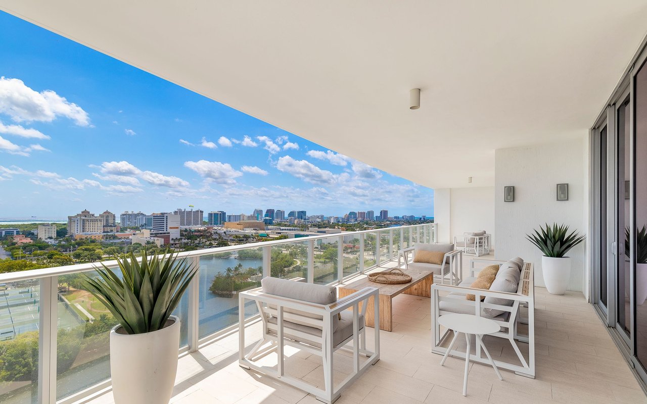 Furnished high-rise balcony overlooking water, greenery, and a broad city skyline.