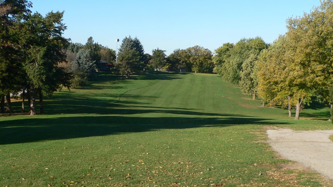 A wide golf course fairway framed by mature hardwood trees under an open sky