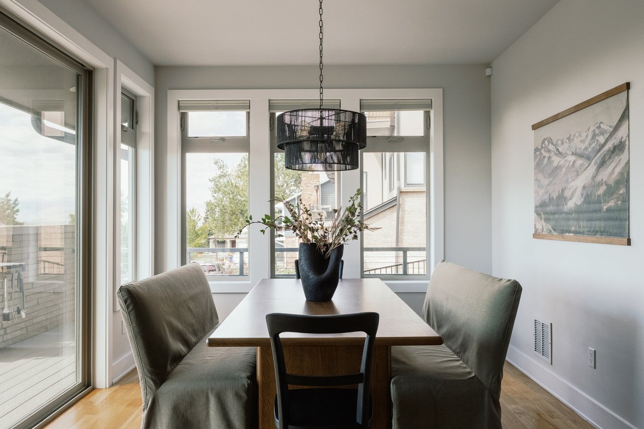 Dining room with a wooden table, upholstered chairs, large windows, and a black pendant light.