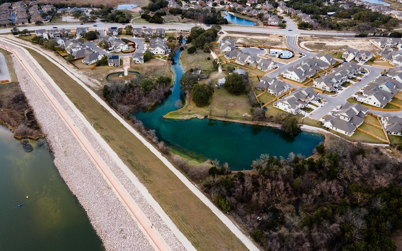 Aerial neighborhood with houses beside turquoise water and a long rock-lined embankment.