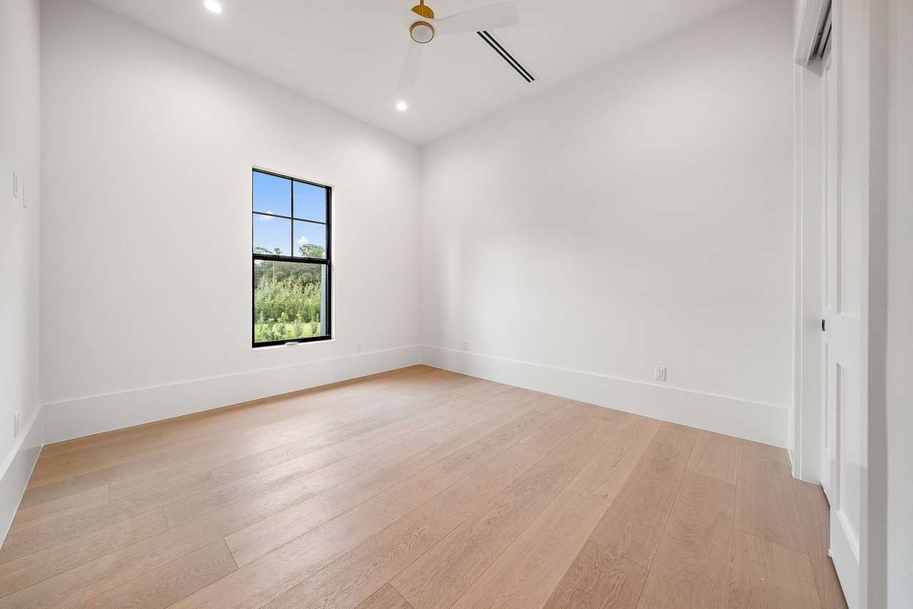 Empty room with light wood flooring, a high ceiling fan, and a window overlooking greenery.