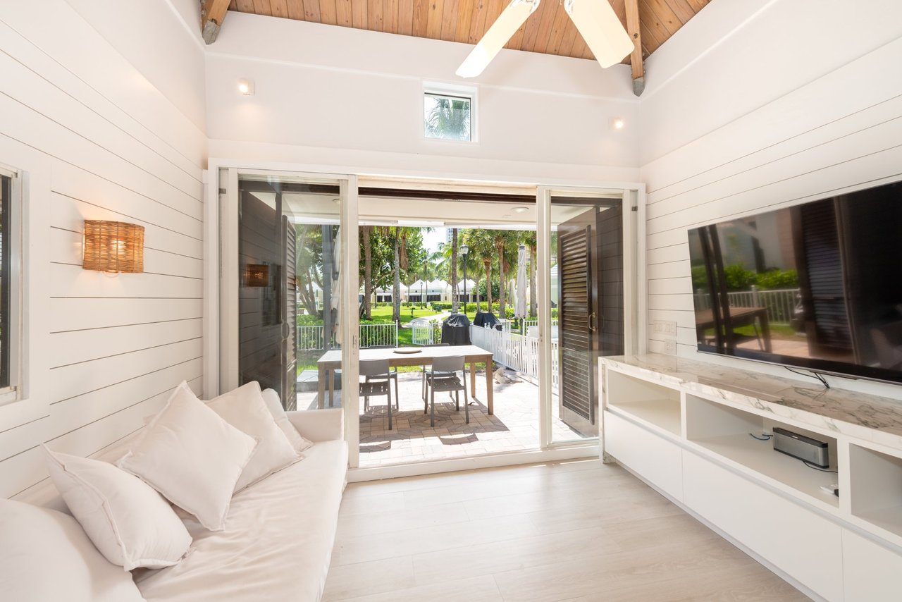 Cabana living room with vaulted wood ceiling, white sofa, and sliding doors to a palm-lined patio.