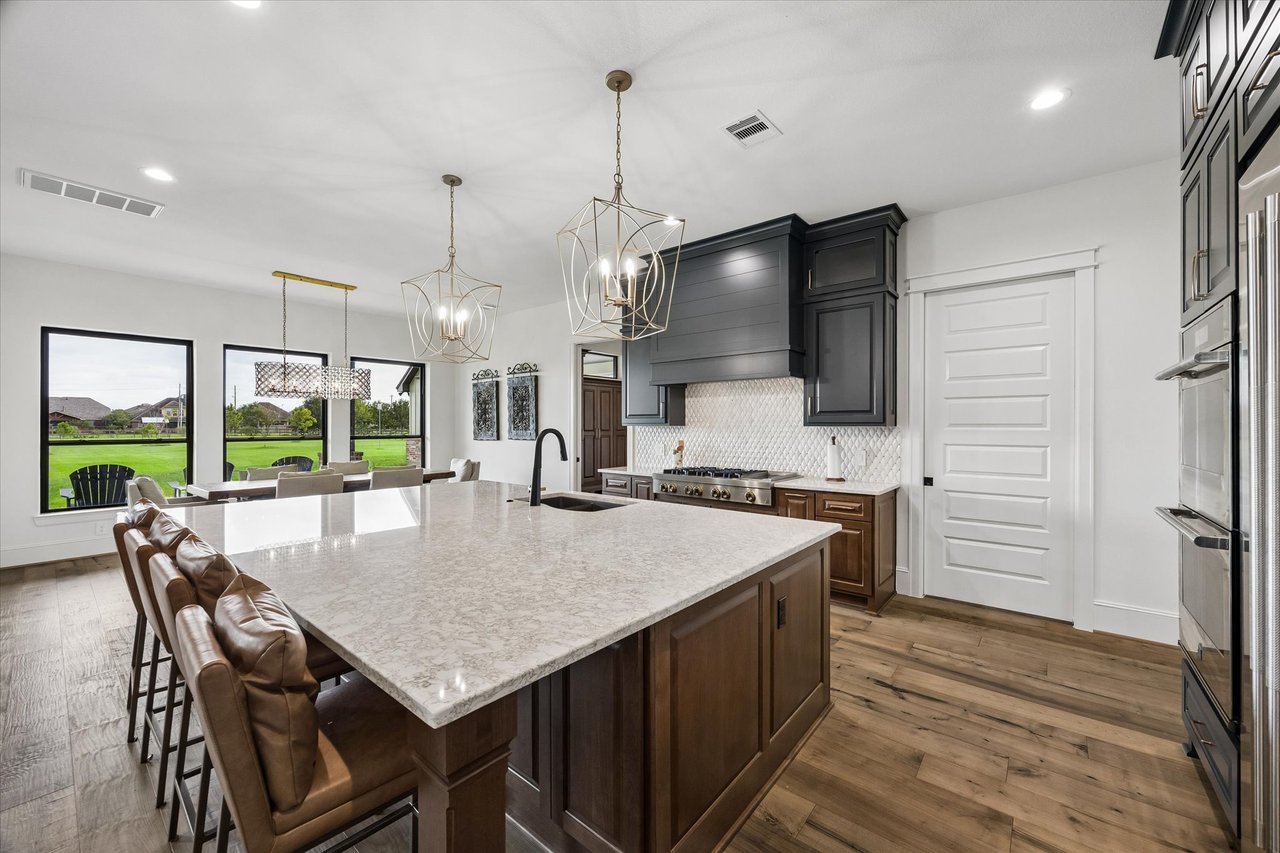 Kitchen with a large stone island, dark cabinetry, leather barstools, and windows overlooking a green lawn.