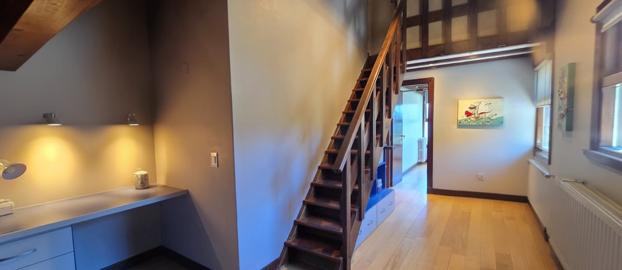 Interior with a dark wooden staircase to a mezzanine, built-in desk, and light wood flooring.