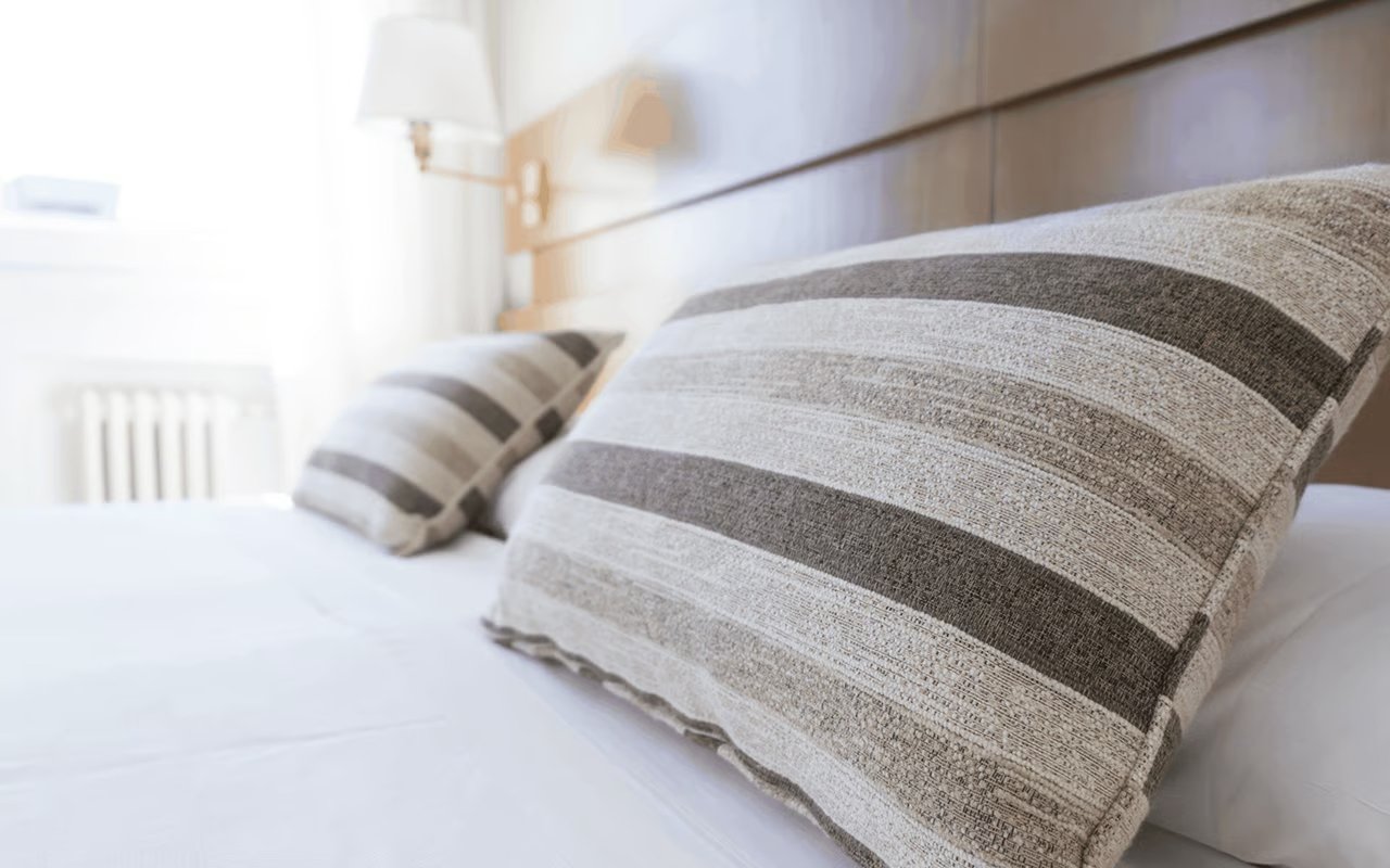 Bedroom bed with white bedding and large gray-and-beige striped pillows.