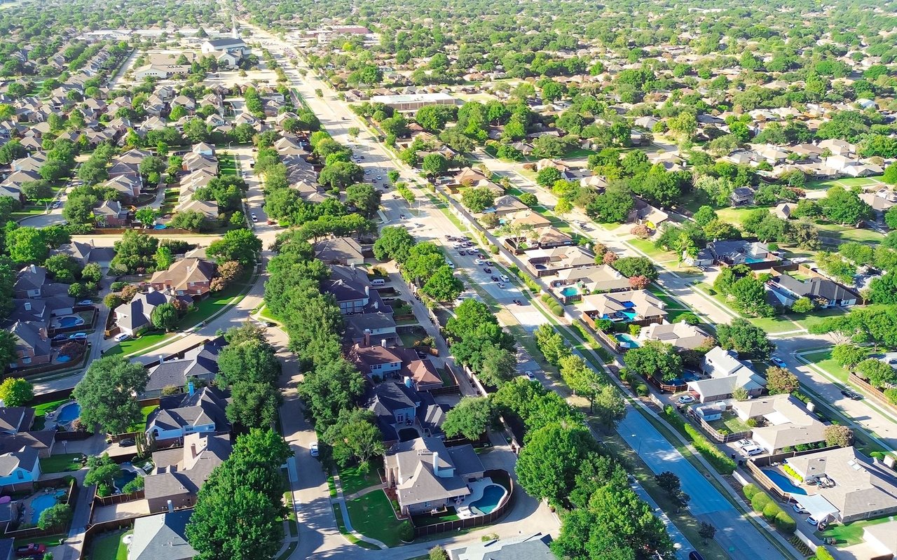 Aerial view of a tree-lined neighborhood with detached homes and streets.
