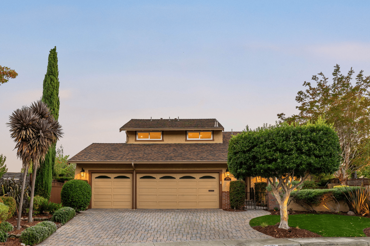 Two-story home with a three-car garage, broad paved driveway, and landscaped front yard at dusk.
