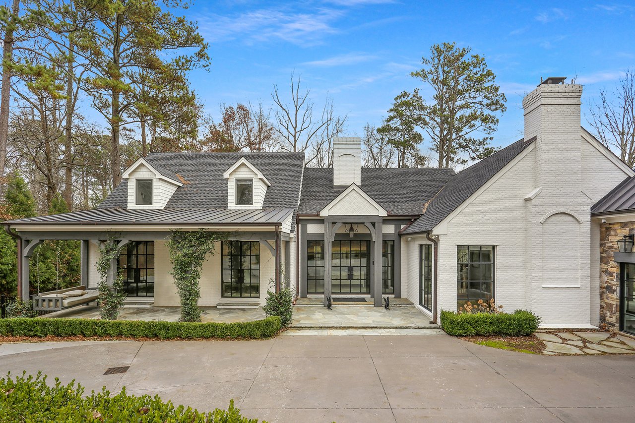White brick home with dark-framed windows, roof dormers, a covered porch, and a broad chimney.