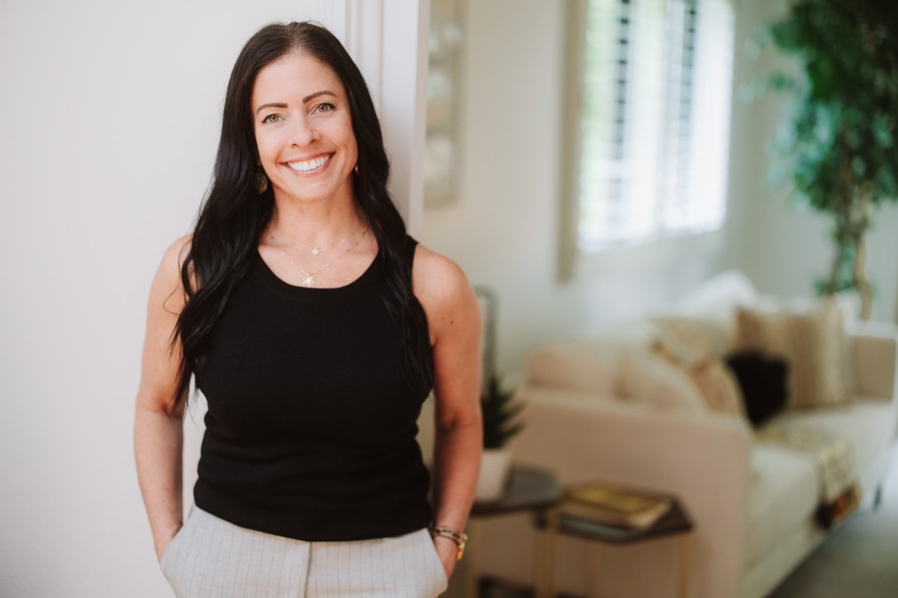 Trisha Sultze smiling in a black sleeveless top in a bright living room.
