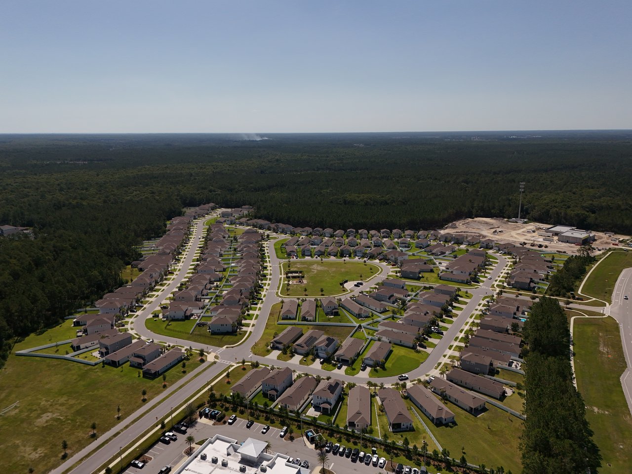Aerial view of a housing development with curving streets, a central green, and surrounding woodland.