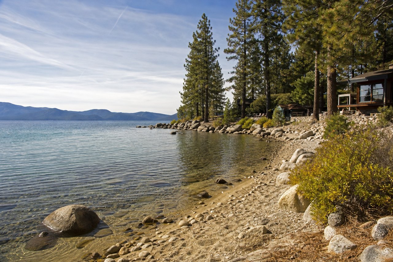 Rocky Lake Tahoe shoreline with clear water, pine trees, and homes along the shore.