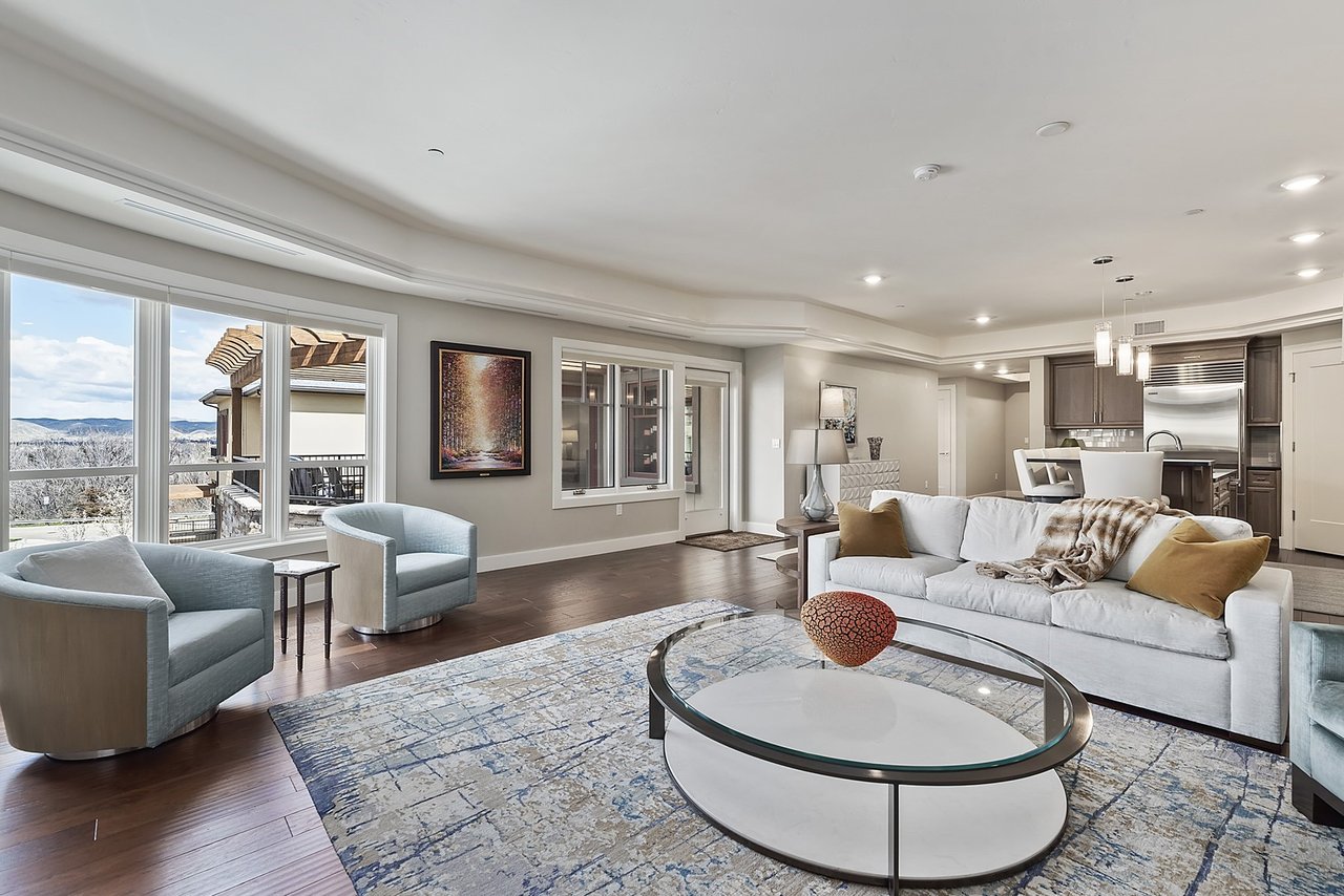 Open-plan living room with white seating, blue armchairs, and large windows overlooking distant hills.