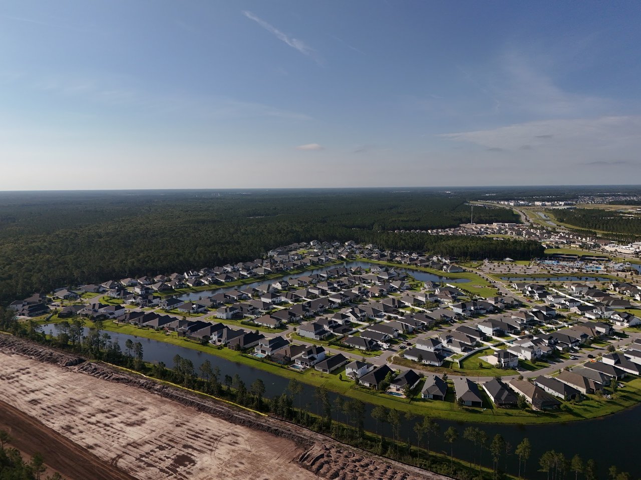 Aerial view of a residential subdivision with ponds, wooded surroundings, and cleared land in the foreground.