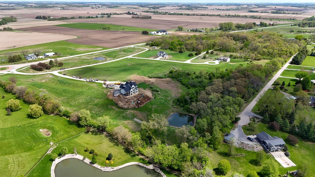 Aerial view of Oak Meadow with winding roads, wooded areas, ponds, and a home under construction.