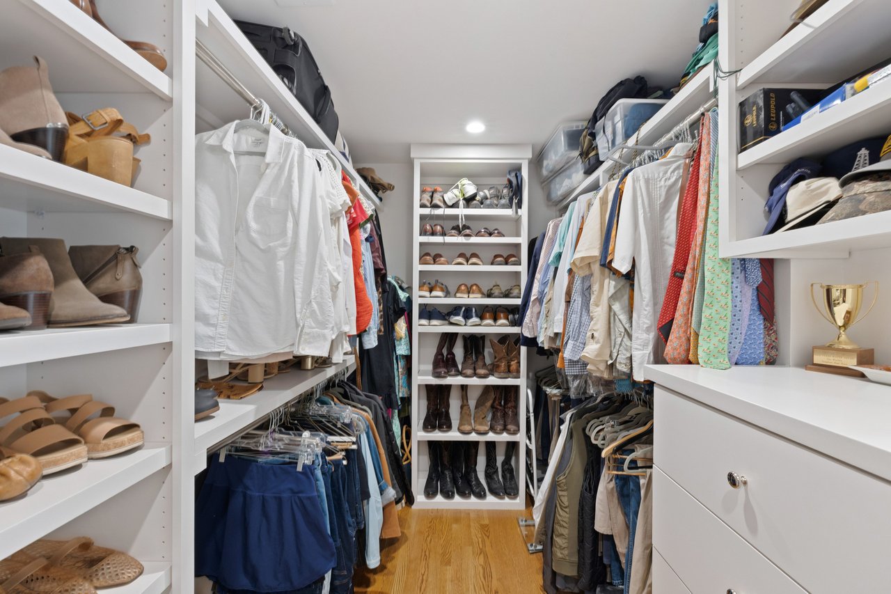 Walk-in closet with built-in shoe shelves, hanging clothes, and a trophy above white drawers.