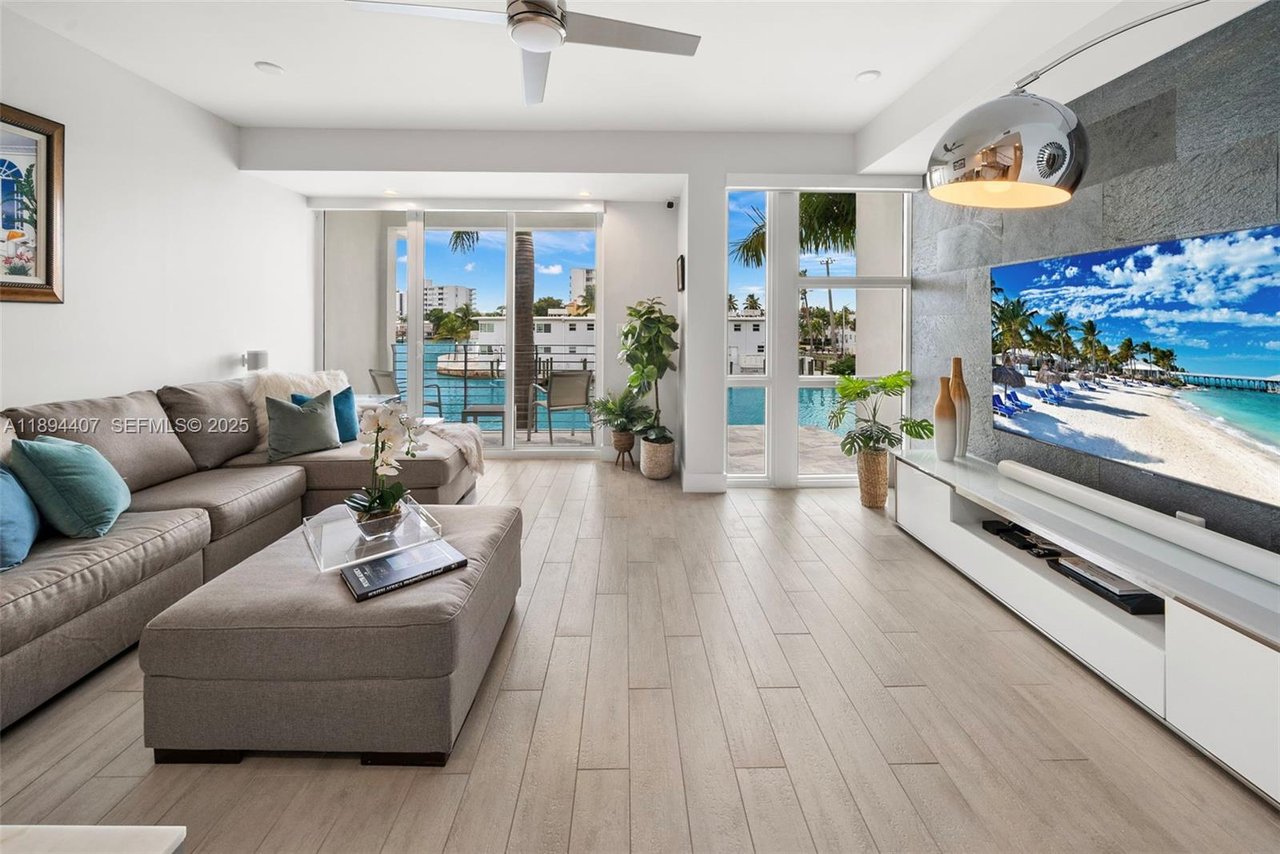 Waterfront living room with a gray sectional, pale tile floors, and canal views through tall windows.