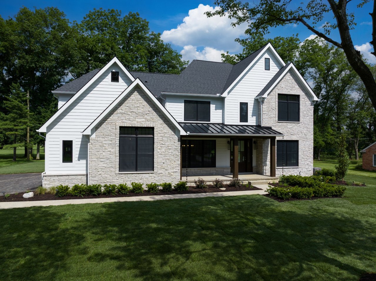 Two-story white-sided house with stone gables, dark windows, and a covered entrance.
